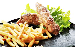 french fries and fried meat with vegetable served on black tray