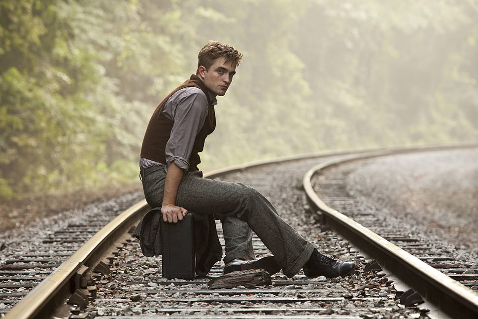 man in grey pants sitting on suitcase in train rails HD wallpaper