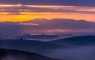 silhouette of mountain covered by fogs during sunset