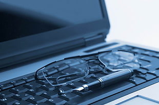 black-framed clear lens eyeglasses in front of fountain pen on laptop