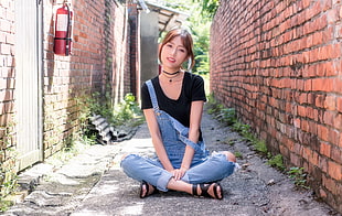 sitting woman in black scoop-neck t-shirt beside brick wall at daytime