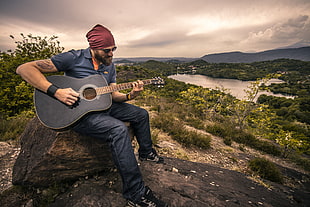 man sitting on rock playing guitar