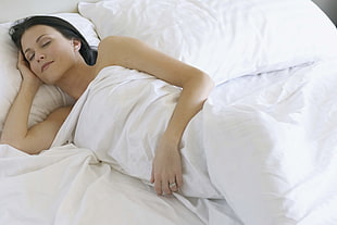 woman lying on bed covered with white blanket