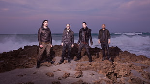 four men band on rocky terrain near ocean
