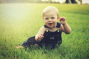 baby in blue dungaree surrounded by grass during daytime