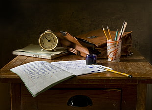 white notebook beside yellow pencil and alarm clock on brown wooden table