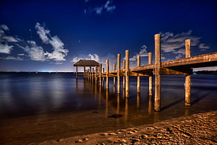 timelapse photo of dock near ocean under clouds during daytime