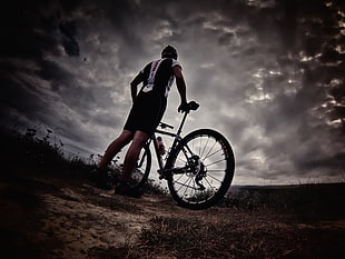 photo of man in bicycle suit holding bicycle over cloudy sky