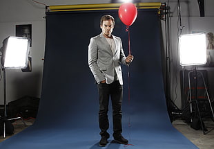 man in gray notch-lapel blazer and black pants holding red balloon