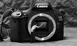 grayscale photo Canon EOS 550D camera body with man cleaning on lens