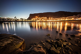 black rocks on body of water near city lights under blue sky during sunset, gran canaria, canary islands HD wallpaper