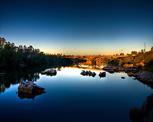 calm river on brown rocks with brown bridge under clear blue sky
