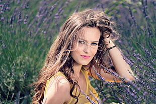 woman wearing yellow sleeveless top with black wavy long hair surrounded by blue cluster flower field