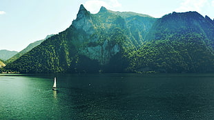 white sail boat on body of water near mountain ranges
