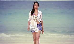 women's white elbow-sleeved blouse with blue denim short shorts walks near sea during daytime