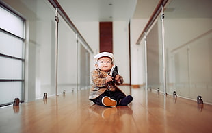 baby in plaid blazer sits on brown wooden flooring in between glass rails