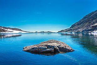 rock formation on body of water near mountain during daytime