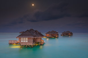 brown and black nipa huts in the middle of ocean illustration HD wallpaper