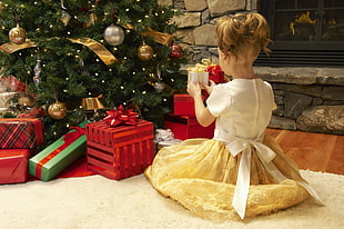 girl wears white and yellow dress holds white gift box near Christmas tree