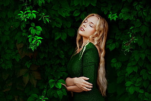 long blonde-haired woman in green top beside green tree
