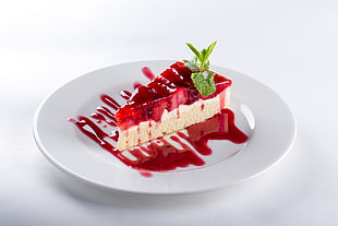 sliced cheesecake topped with strawberry syrup on round white ceramic saucer