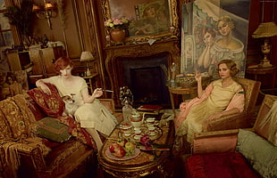 two women sit inside living room painting