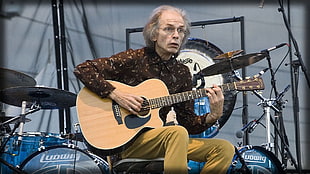 man in brown dress shirt playing acoustic guitar near drum set