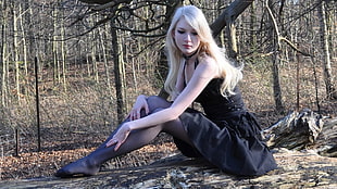 woman wearing black sleeveless dress sitting on ground near trees