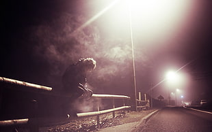person sitting on bamboo street fence at night