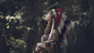 woman in white, red, and black feather headdress looking up