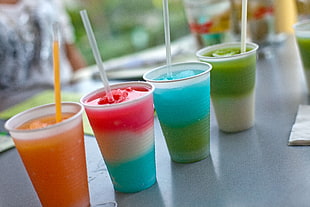 macro shot photography of four cocktails smoothies in white plastic cups during daytime