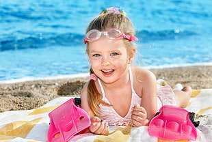 girl wearing white swimsuit and pink framed goggles near body of water