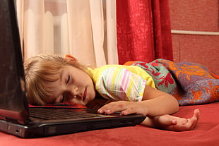 blonde girl wearing yellow top lying on red surface near opened laptop computer