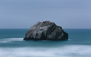 brown rock in the middle of ocean under cloudy sky at daytime