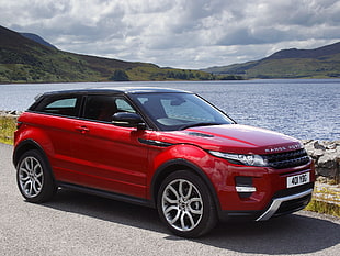 red Land Rover Range Rover park on road near body of water during daytime