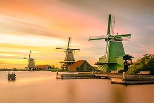 three windmills near body of water at sunset