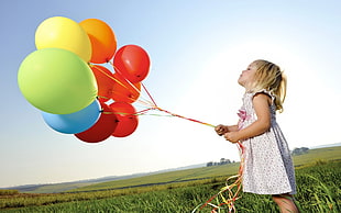 girl in white dress holding assorted-color balloons