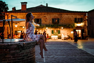 woman wearing white and red floral dress sitting on brown brick surface in tilt shift lens shot