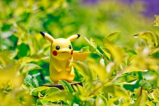 Shallow photography on Pikachu figure from Pokemon standing on plants during daytime