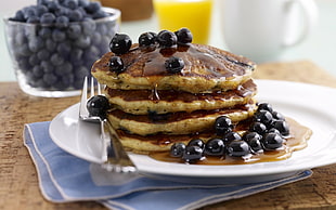 pancake with blueberries and stainless steel fork on round white ceramic plate
