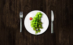 green grapes on white ceramic plate with spoon and fork beside on brown wooden table