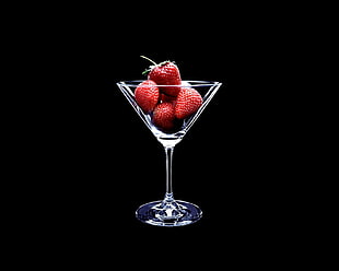 cocktail glass filled with strawberries covered by dark surface