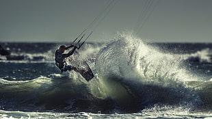 man hanging on rope on wave body of water photo