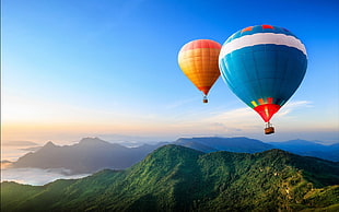 blue and orange air balloon flying on top of mountain