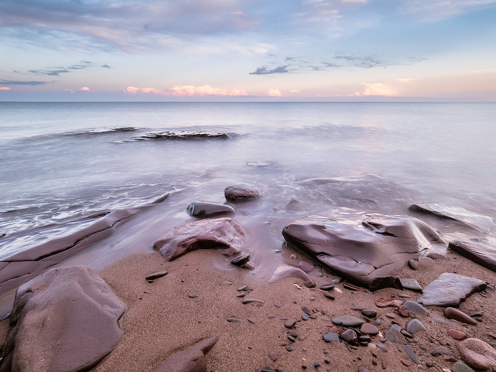 stone on sand beside seaside under cloudy blue sky during daytime HD wallpaper