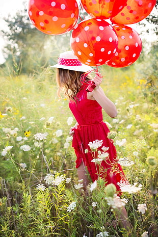 portrait photography of woman in red dress holding red balloons