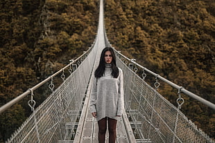 woman wearing gray sweatshirt standing in the middle of metal hanging bridge