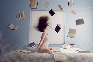 woman sitting on bed with books flying
