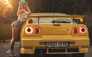 woman in white top and blue denim short shorts beside yellow car