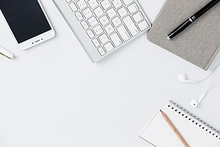 white smartphone beside wireless Apple keyboard with mouse and notebook